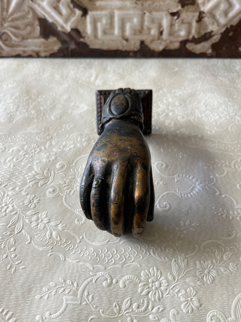 "Antique French cast iron 'Hand of Fatima' door knocker with a decorative ruffled cuff, holding a ball, can mounted on a rustic wooden door. or modern door"