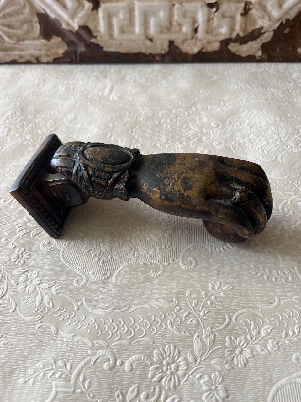 "Antique French cast iron 'Hand of Fatima' door knocker with a decorative ruffled cuff, holding a ball, can mounted on a rustic wooden door. or modern door"